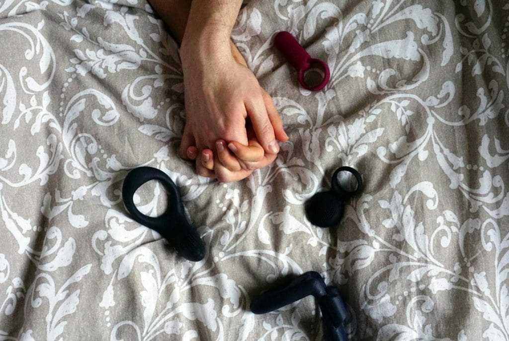 sex toys on a bed with hand holding each other